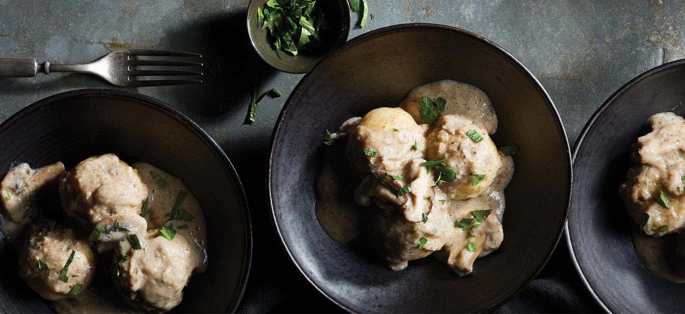 German Potato Dumplings with Mushroom Gravy in black ceramic bowls with a smaller bowl of chopped parsley