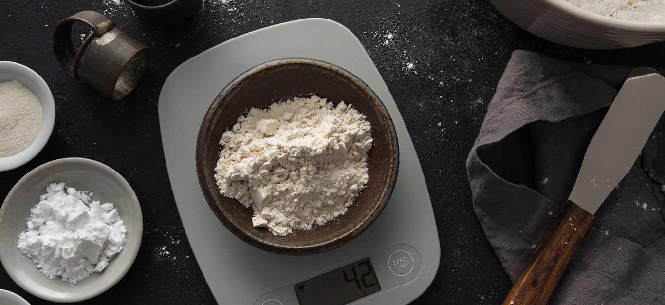 oat flour in a bowl on a kitchen scale, beside a smaller bowl of potato starch, with a larger bowl of whole grain gluten-free flour off to one side