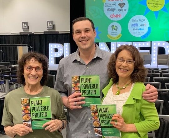 Brenda Davis, RD; Vesanto Melina, MS, RD; and Cory Davis, MBA, P.Ag together at the 2023 Plant-Based Expo Conference holding up the book they co-authored, Plant-Powered Protein