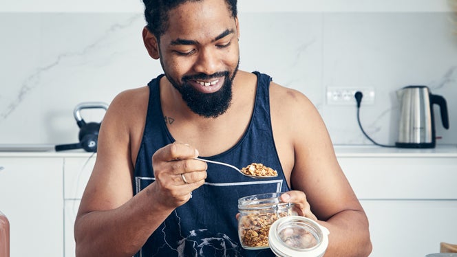 A fit young man is in his kitchen happily spooning rolled oats into a bowl to make a healthy plant protein-rich meal