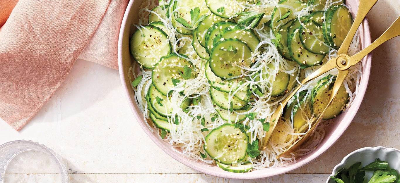 Cucumber and Glass Noodle Salad in a light pink serving bowl with gold metal tongs