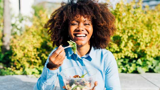 African American woman smiling in the sunshine eating a salad