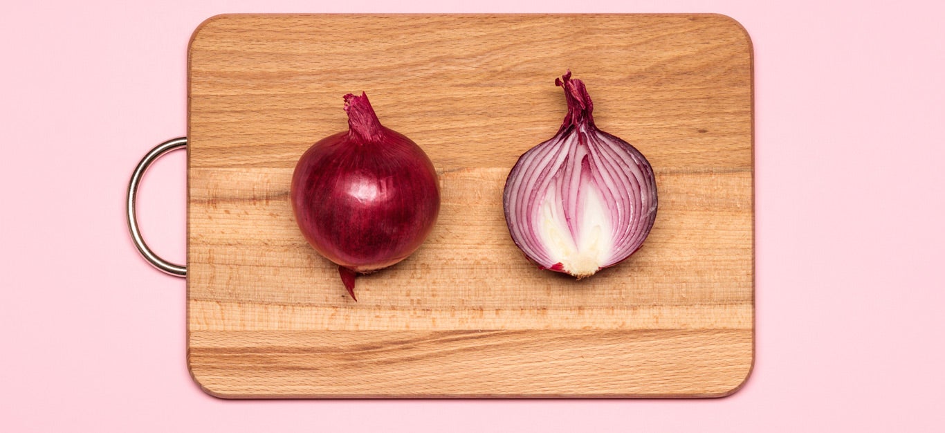 two halves of a red onion lying on a cutting board, with one half facing cut side down and the other half facing cut side up, on a solid pink abstract background