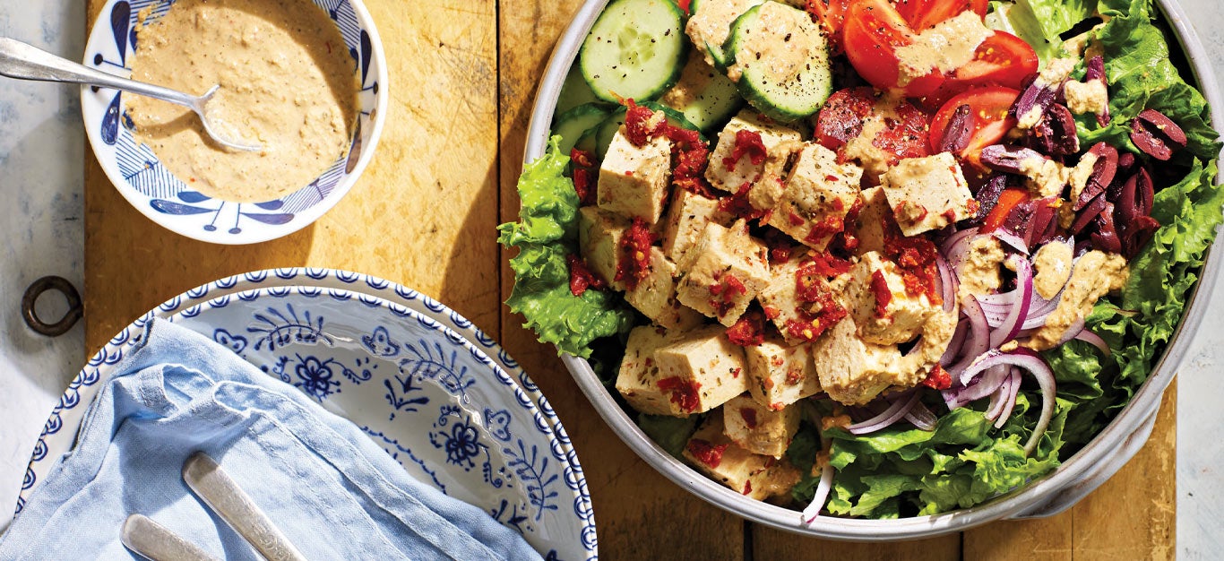 Greek Salad with Sun-Dried Tomato Tofu Feta in a white serving bowl on a wooden tabletop