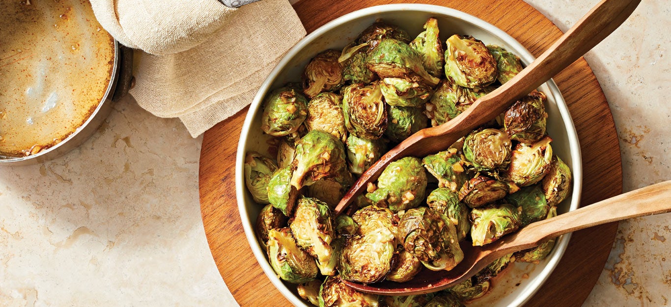 Sweet and Spicy Air-Fried Brussels Sprouts in a white bowl with wooden serving spoons