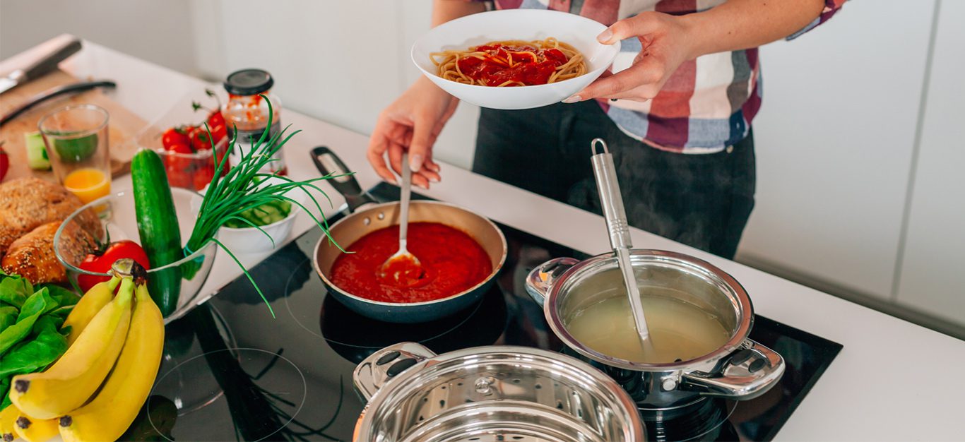 Woman standing over a stove adding pasta cooking water to jarred pasta sauce to make it better