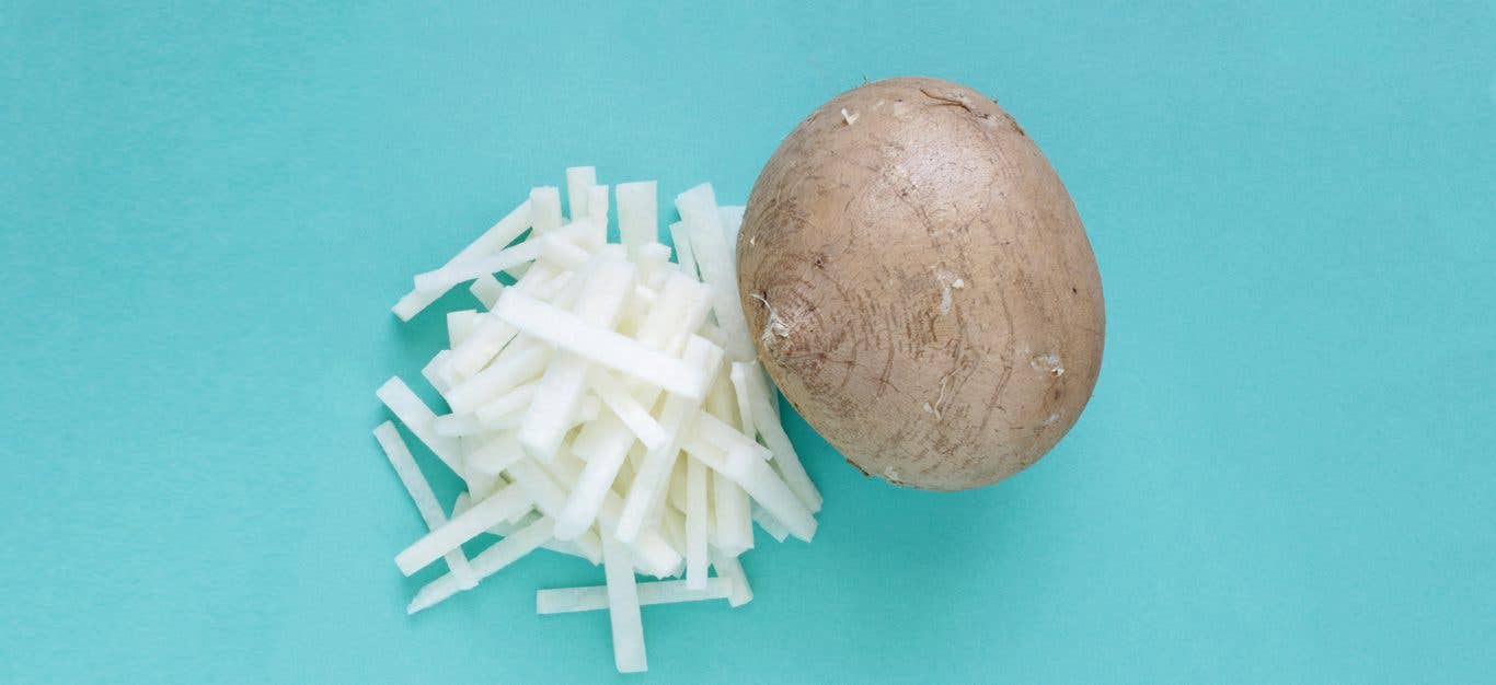 A whole bulb of the root vegetable jicama, on a light blue background, with matchstick-cut slices of peeled jicama beside it