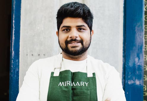Headshot of NIRVAAN THACKER in a white shirt and green apron