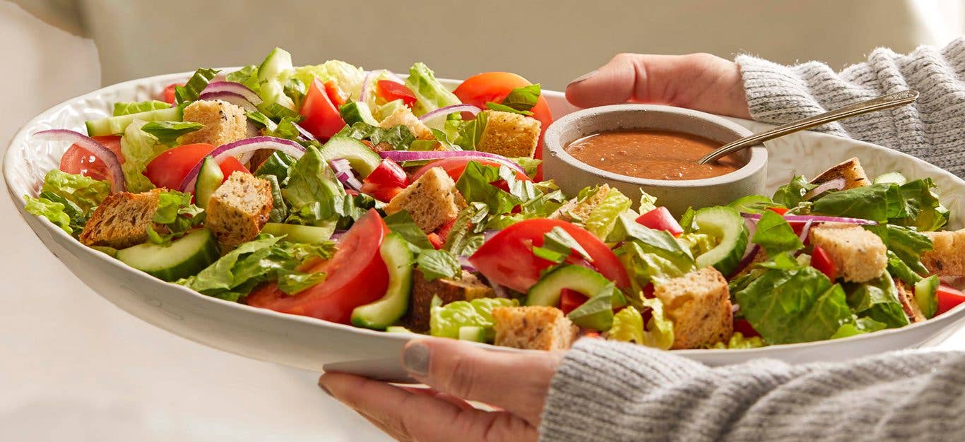 Tuscan Panzanella with Sun-Dried Tomato Vinaigrette on a white platter being held in a woman's arms