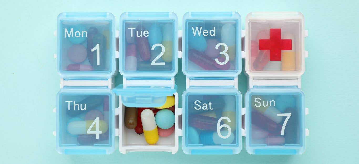 A weekly medication holder is stuffed full of pills against a blue background