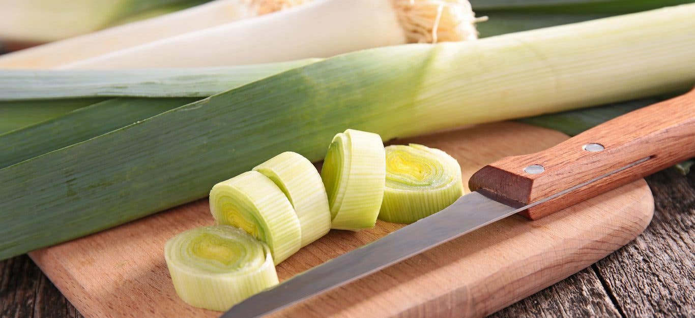 close up shot of sliced leeks on a cutting board beside whole leeks, with a knife to the side
