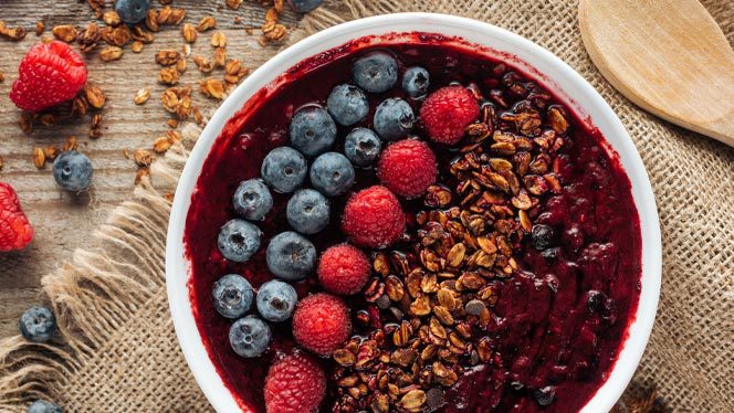 Purple smoothie bowl with rows of blueberries, raspberries, and granola on a burlap background