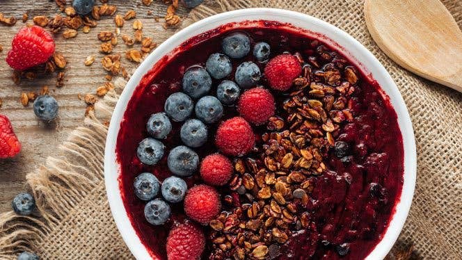 smoothie-bowl Purple smoothie bowl with rows of blueberries, raspberries, and granola on a burlap background