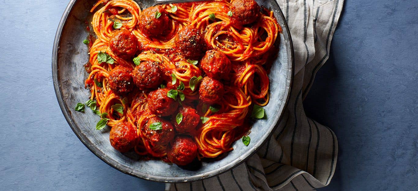 Big plate of vegan spaghetti with vegan meatballs and red sauce served in gray-blue bowl and table