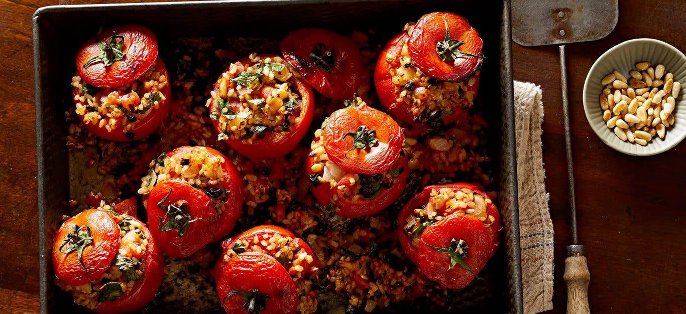 Greek-Style Vegan Stuffed Tomatoes in a baking pan, with filling spilling out