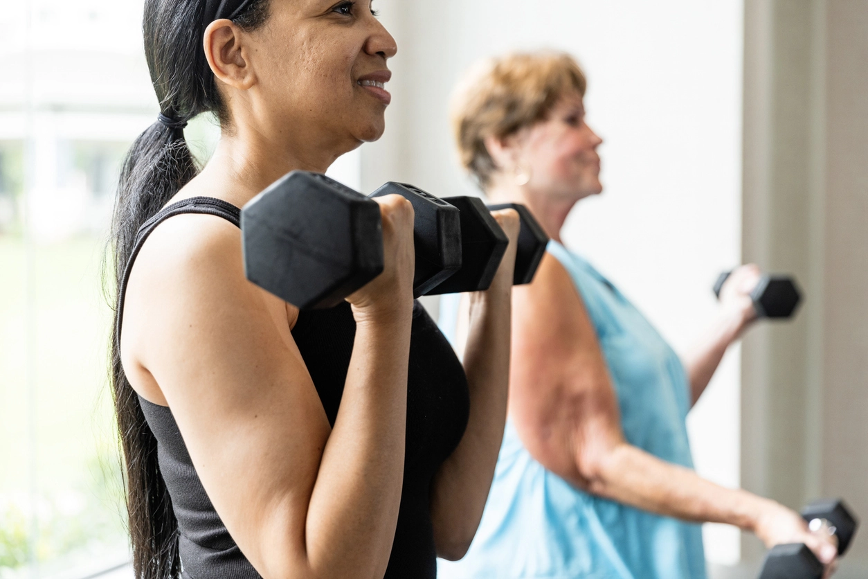 A middle-aged woman and senior woman lifting weights in a gym