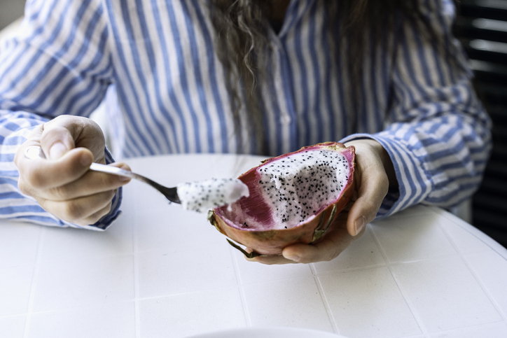 someone scooping out dragon fruit flesh with a spoon