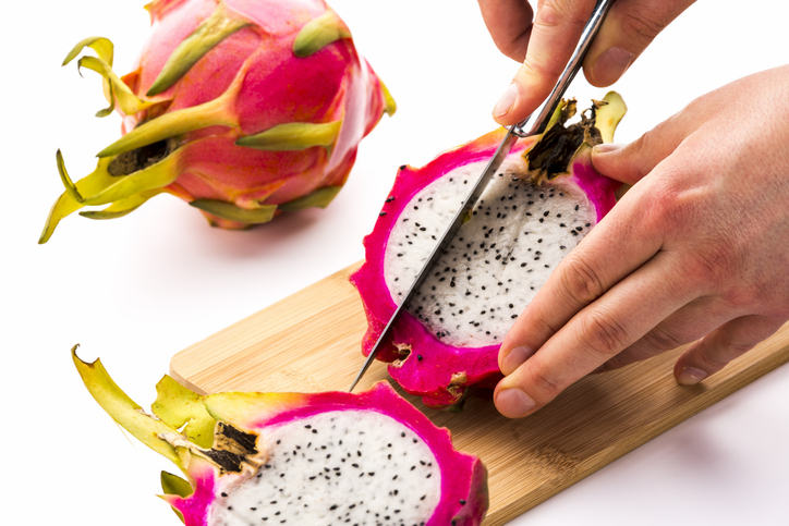 Hands slicing half a dragon fruit into wedges on a cutting board