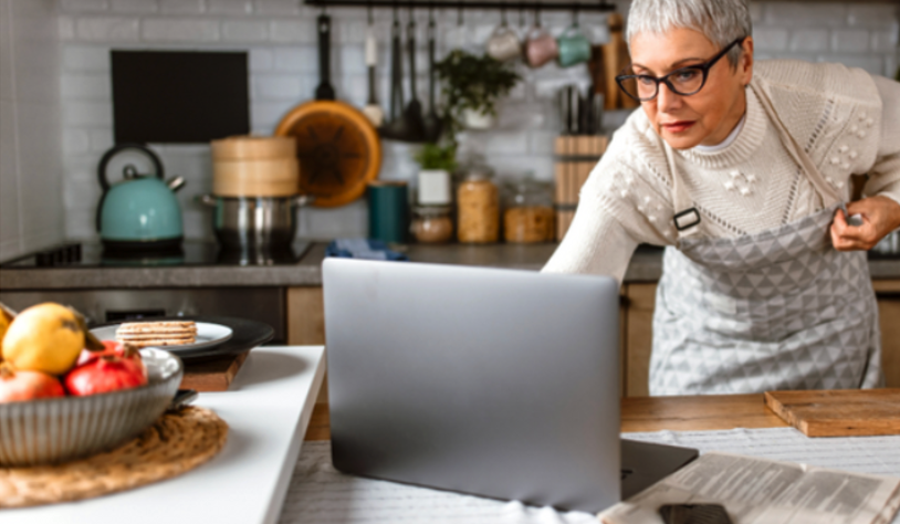 Older woman in the kitchen reading cooking instructions on her laptop