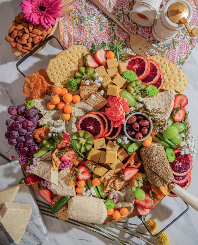 Vegan cheese board by Chef Bailey Ruskus with a colorful array of plant based ingredients including homemade vegan soft cheese and seasonal fruits and fresh herbs and edible flowers