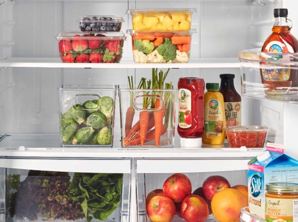 an open fridge stocked with some healthy whole plant based ingredients, including fresh fruit, pure maple syrup, almond milk, and condiments