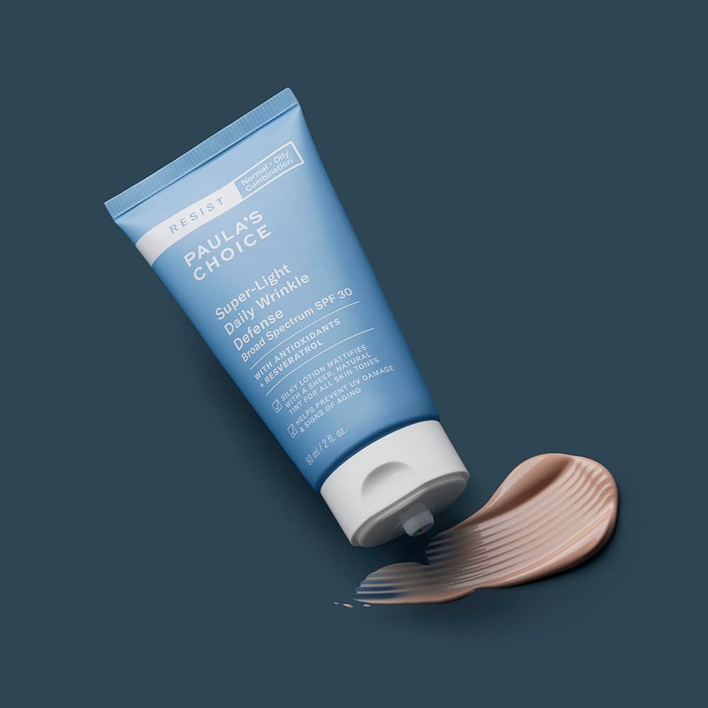 A bottle of Paula's Choice Super Light Daily Wrinkle Defense SPF on a dark blue background, with some of the tinted sunscreen smudged beneath the open cap
