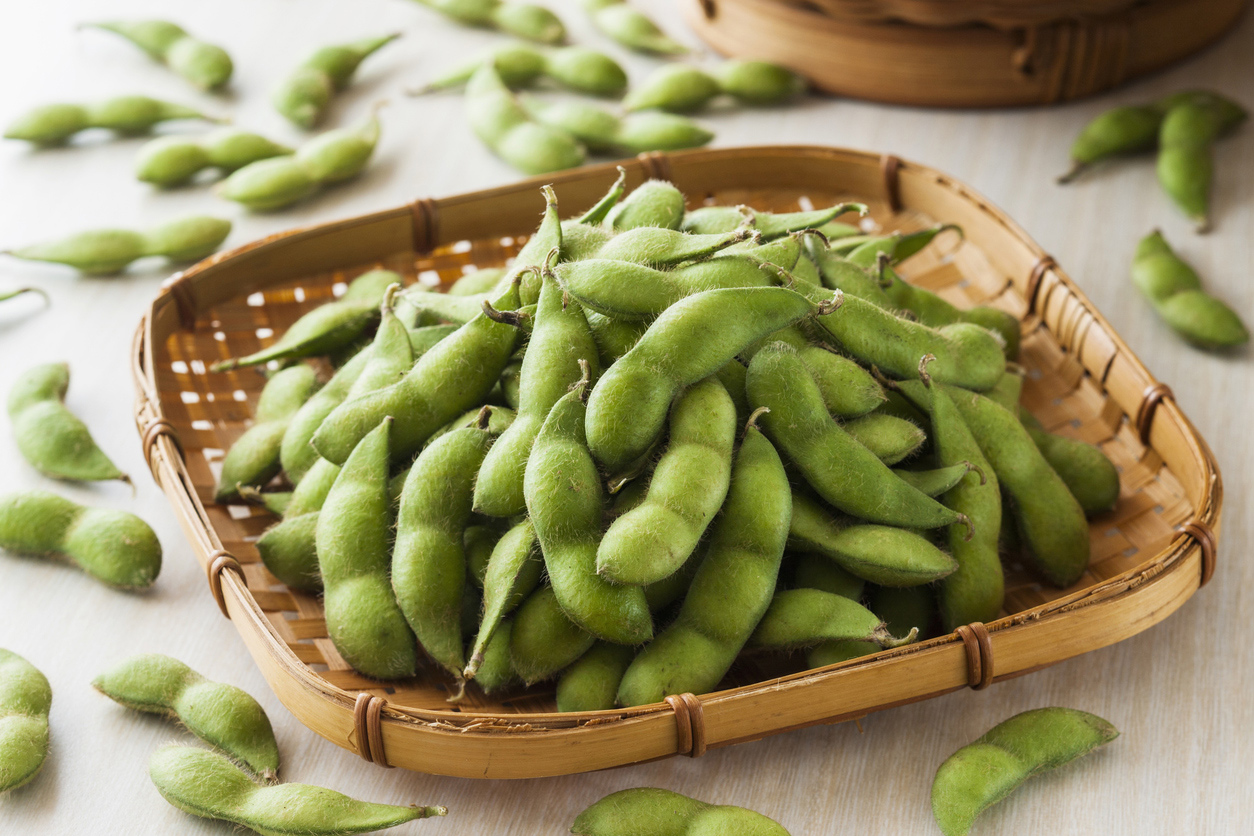 A pile of fresh or steamed edamame in a woven bamboo tray