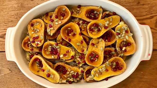 roasted honeynut squash in a casserole dish, sprinkled with pomegranate seeds and pepitas