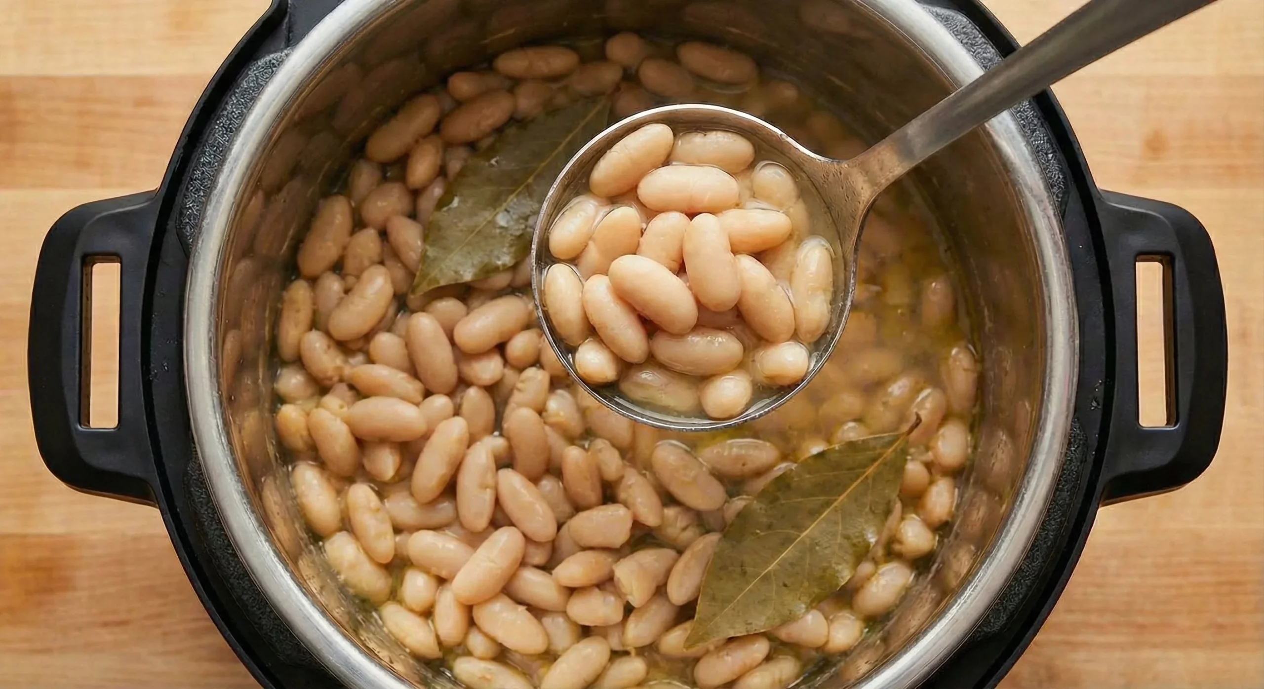 top down view of Instant Pot cannellini beans, with the Instant Pot visible below a ladle full of the cooked beans
