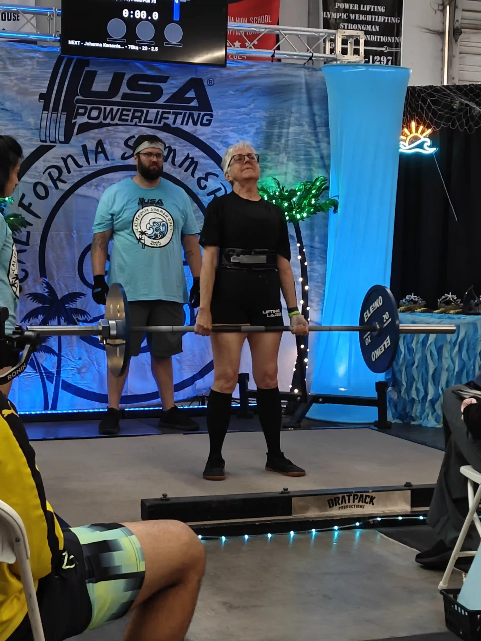 Vegan nun Sister Pat Farrell stands onstage at a weightlifting competition, deadlifting