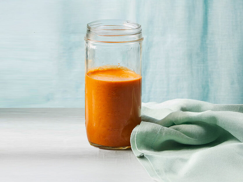 Vegan Queso Sauce in a glass jar, with a pale blue curtain in the backgroujd