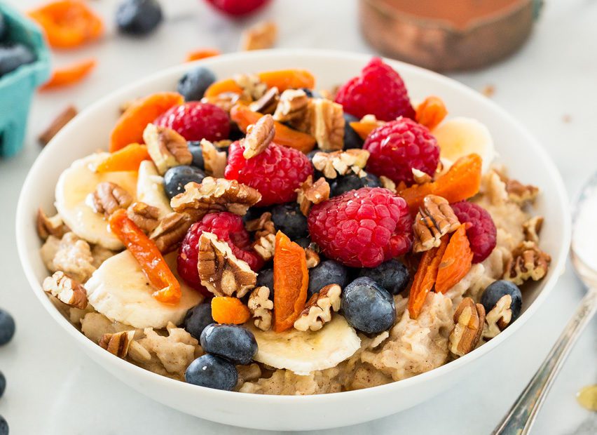 A healthy bowl of oatmeal with raspberries, blueberries, banana slices, and walnuts