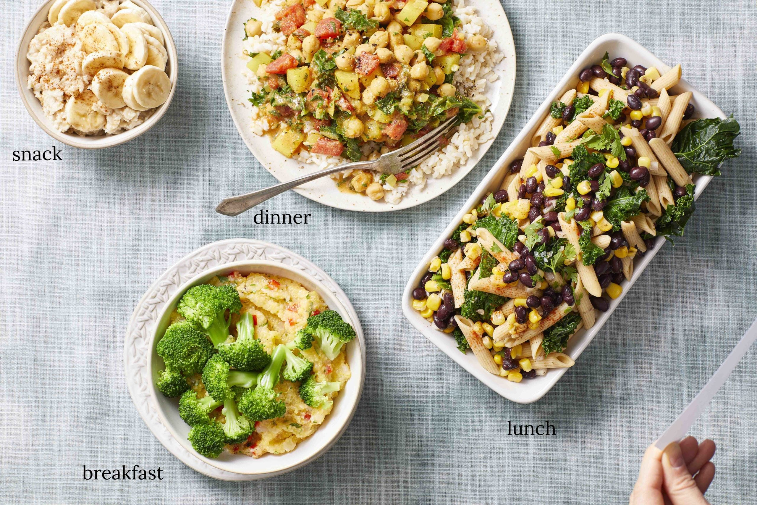 Day 5 of weekly vegan meal plan - banana oatmeal in a bowl next to a bowl of chickpea curry kale stew and a rectangular dish of Tex-Mex pasta salad. At the bottom, a bowl of polenta and broccoli 