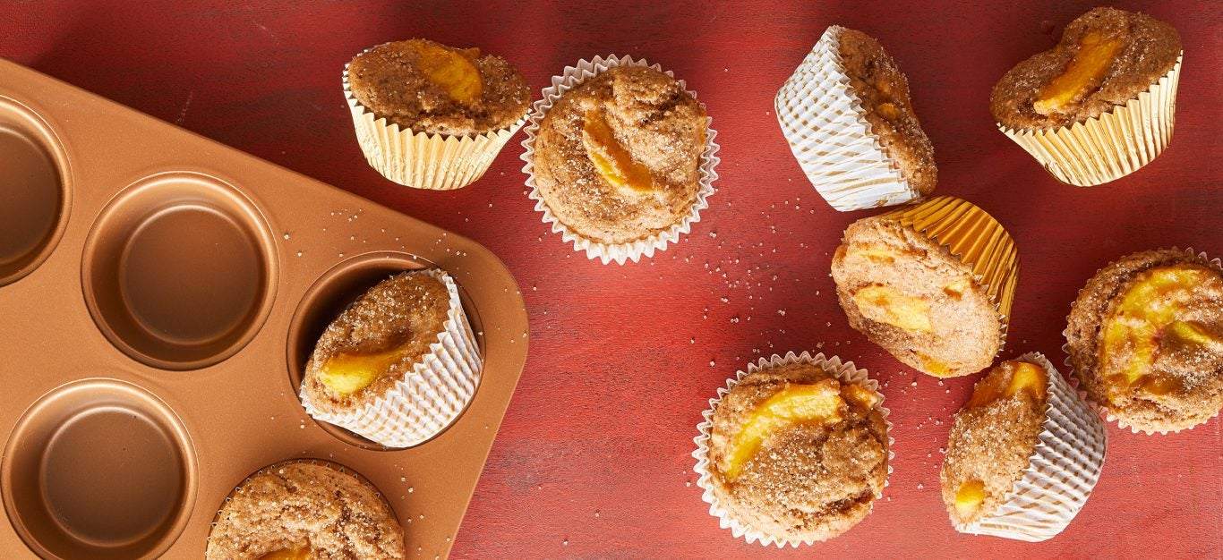 Ginger-Peach Breakfast Muffins on a red table next to a muffin tray