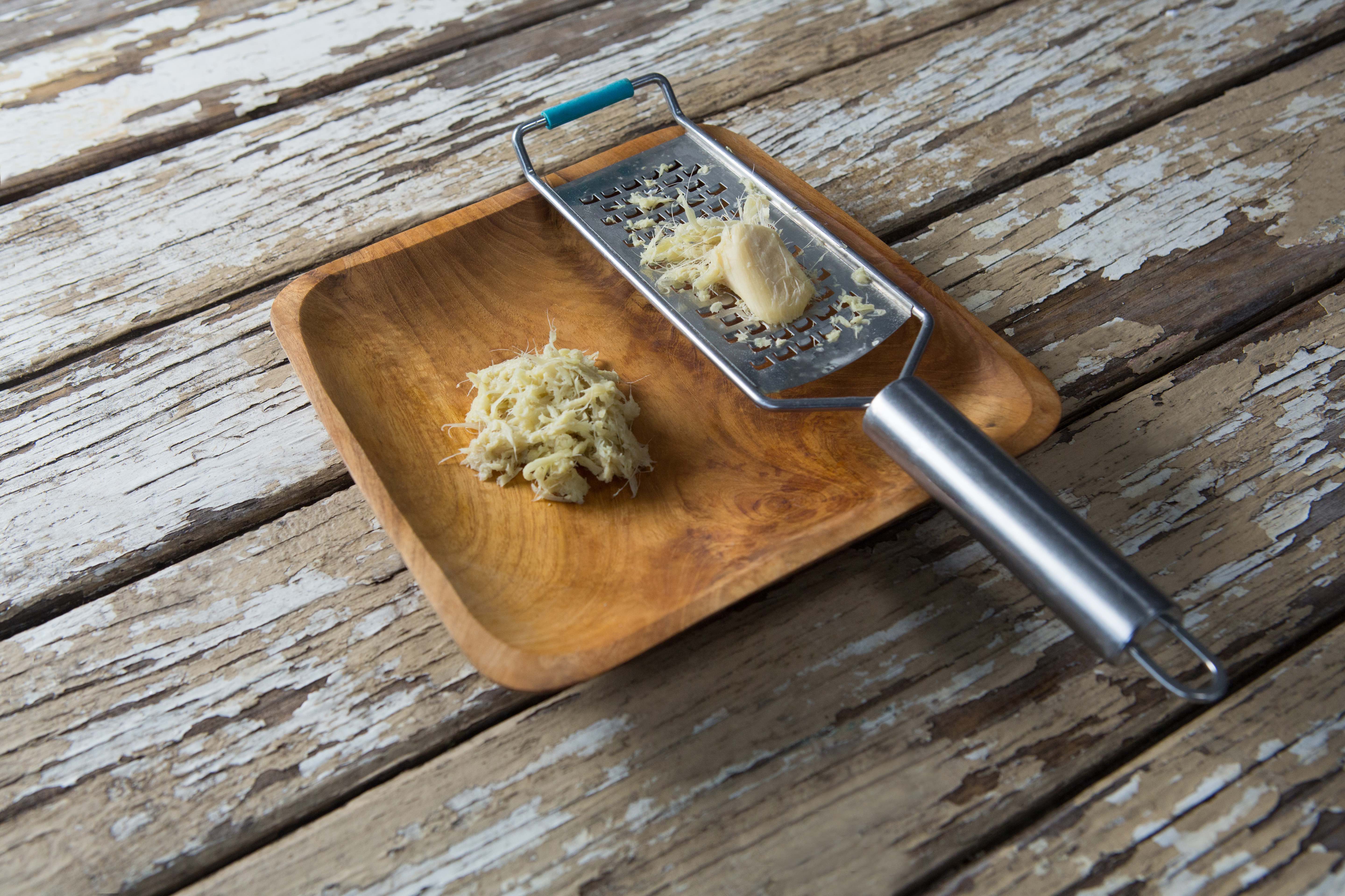 Steel grater and ginger in wooden plate on weathered table