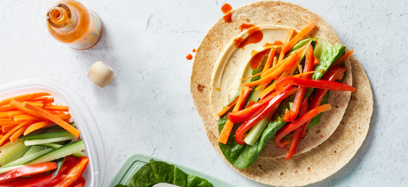 Super-Simple Hummus Veggie Wraps on a white countertop with a bottle of hot sauce