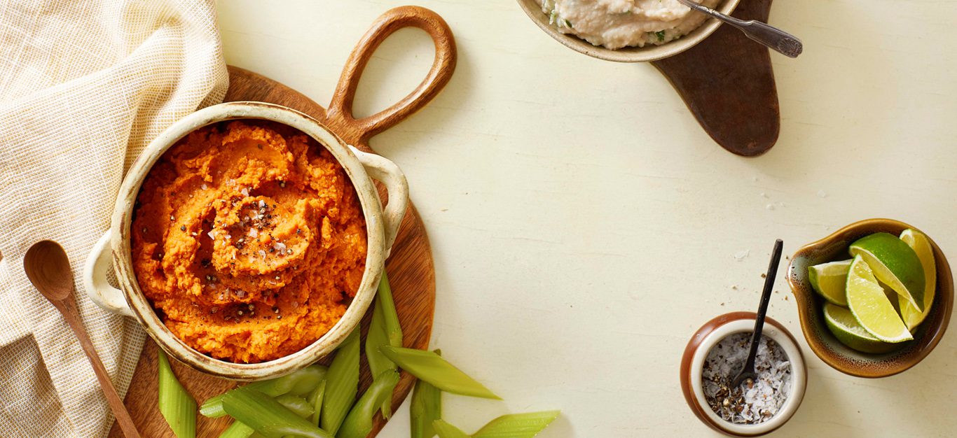 A table with a bowl of harissa roasted hummus, along with edamame and a ramekin of sliced limes