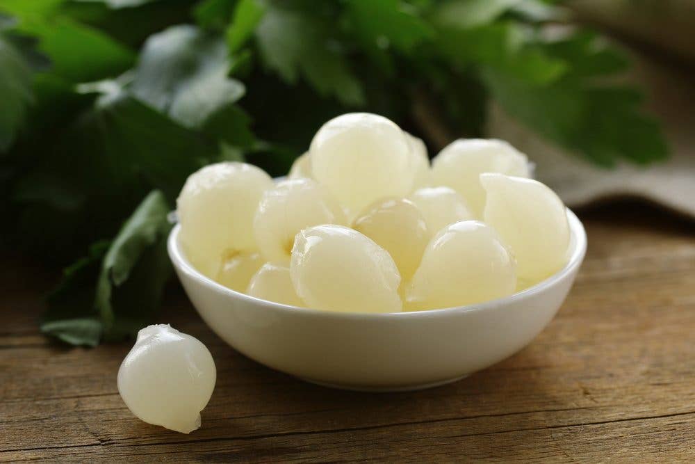 A bowl of peeled pearl onions in a white bowl on a table