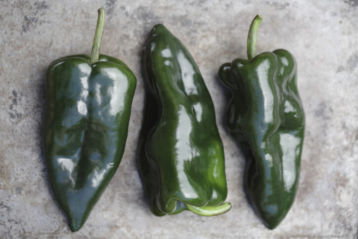 Three poblano chile peppers laid side by side on a marble or concrete countertop