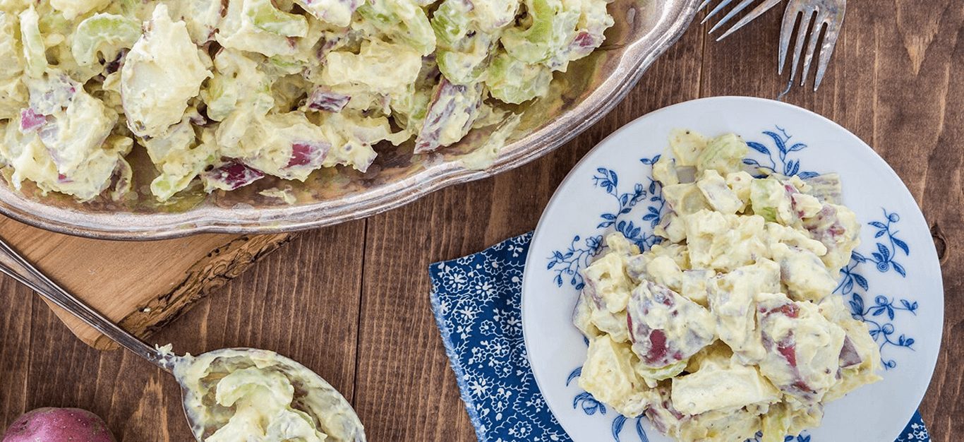 A plate of potato salad in front of a large serving dish full of potato salad