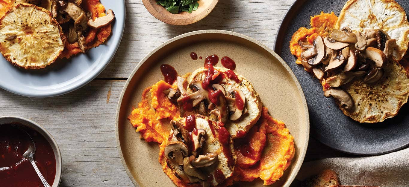 Roasted Celeriac Steaks with Mushrooms and Sweet Potato Mash on a tan plate on a wooden tabletop