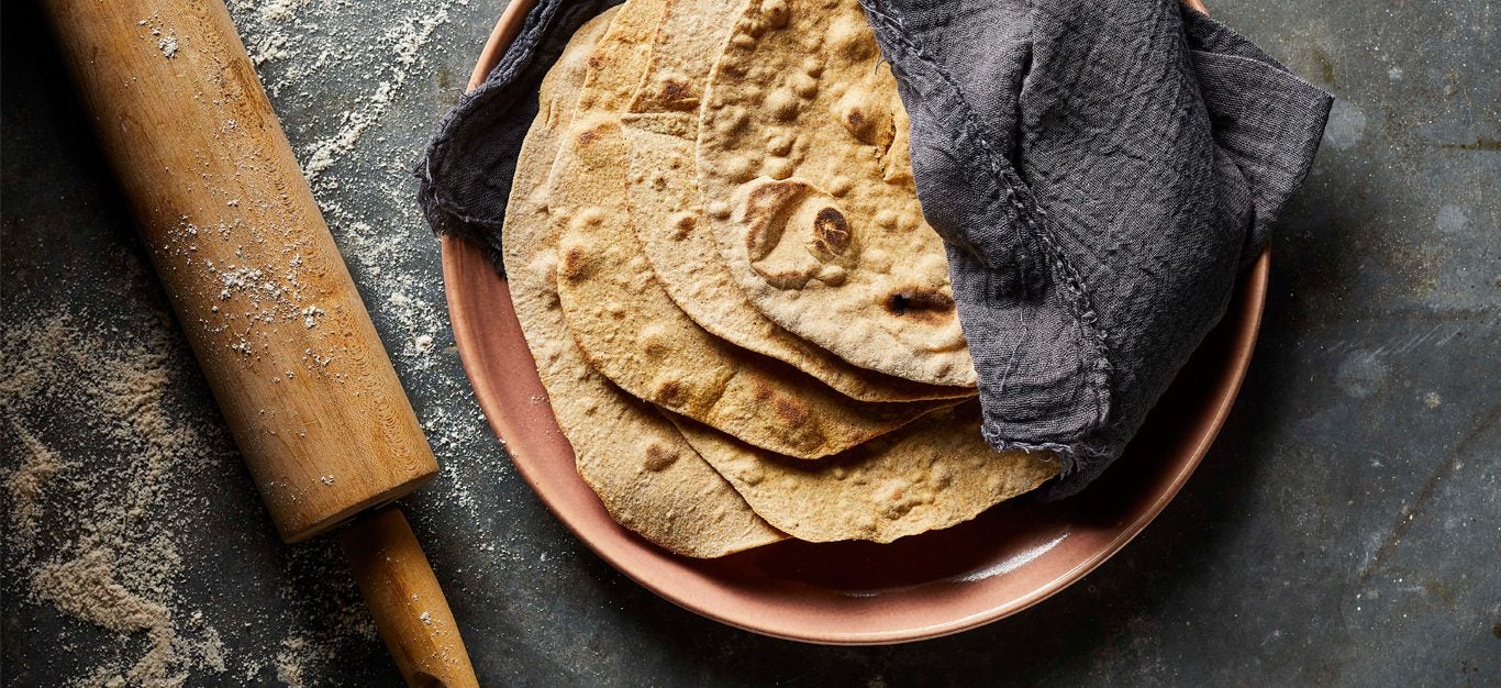 Whole Wheat Flour Tortillas on a pink plate next to a rolling pin sprinkled with flour