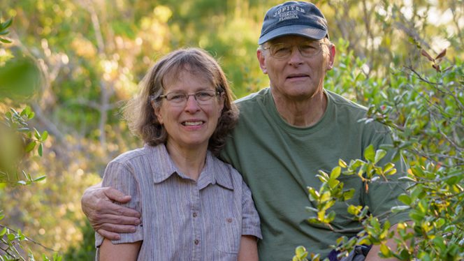 Yolanda and Jim Breidenbaugh pose together in a forested outdoor setting