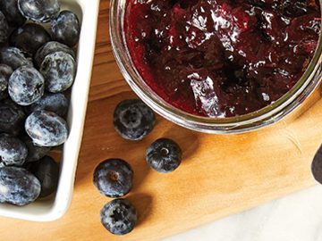 A small carton of blueberries beside a mason jar of homemade jam on a cutting board