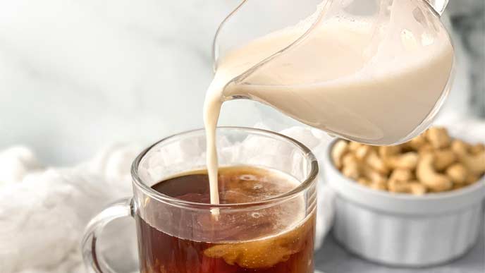 Cashew creamer being pouring from a measuring cup into a glass of coffee