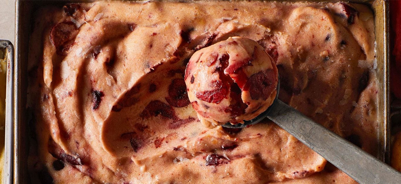 Close-up shot of pink-hued almond cherry nice cream, with visible bits of cherries, and an ice cream scoop