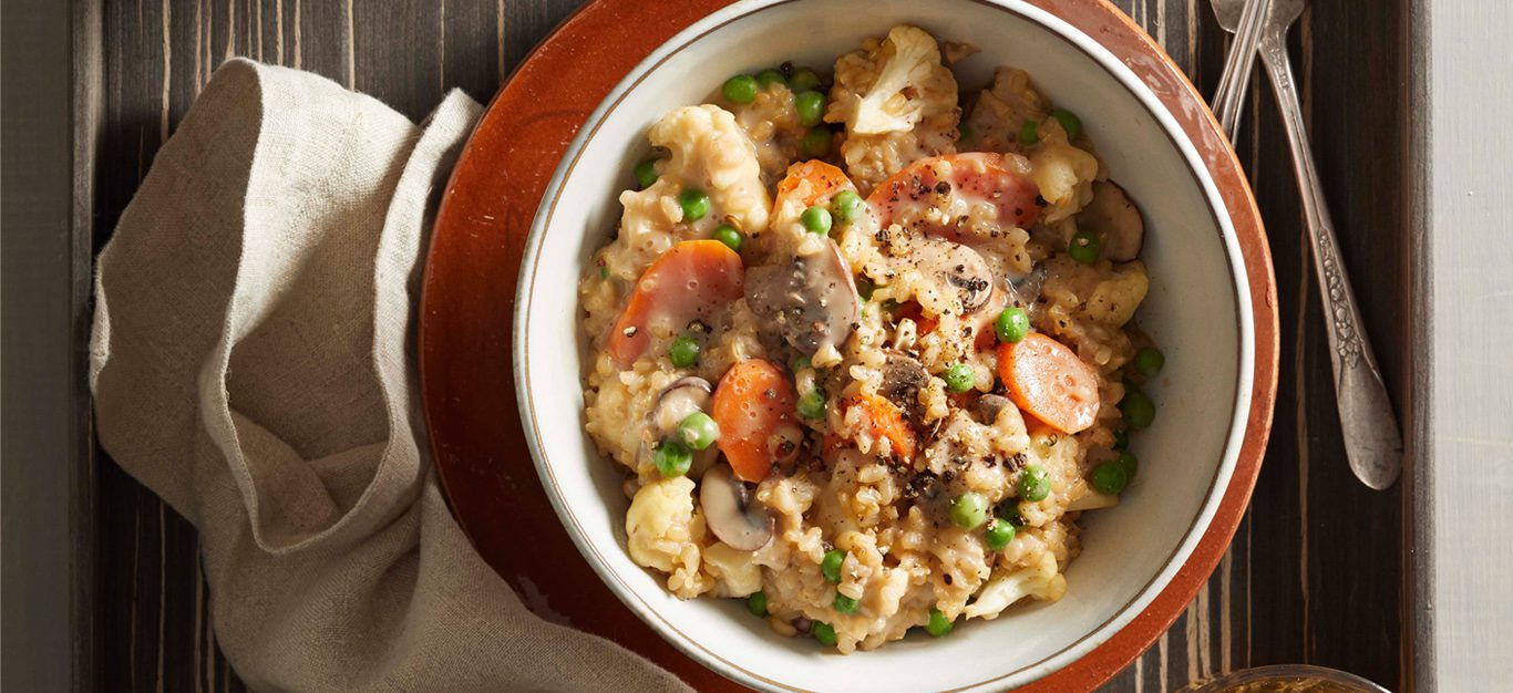 creamy vegan risotto with mushrooms, carrots, and peas, in a white bowl on a red plate