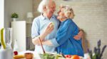 An elderly couple hug each other in the kitchen