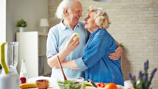 An elderly couple hug each other in the kitchen