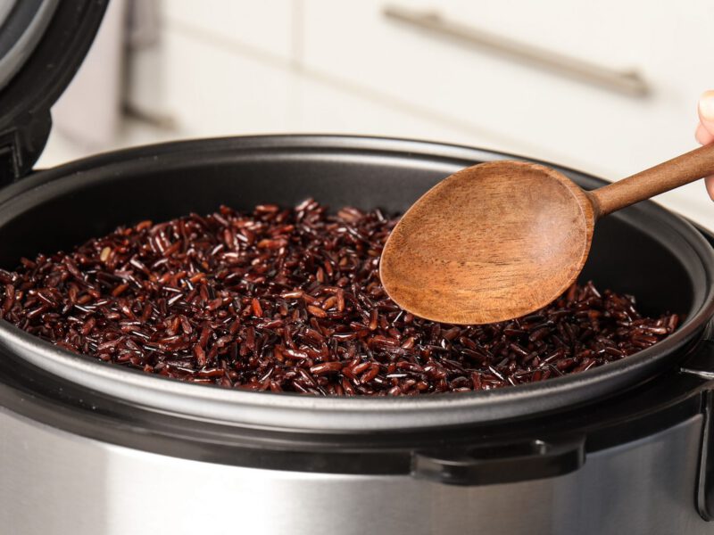 A woman's hand holding a spoon reaches into an instant pot full of wild rice